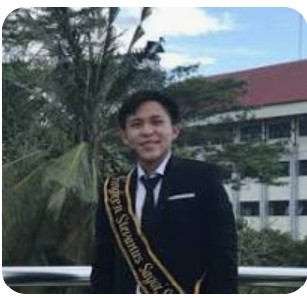 Fingken in a suit wearing a graduation sash embroidered with his name.
